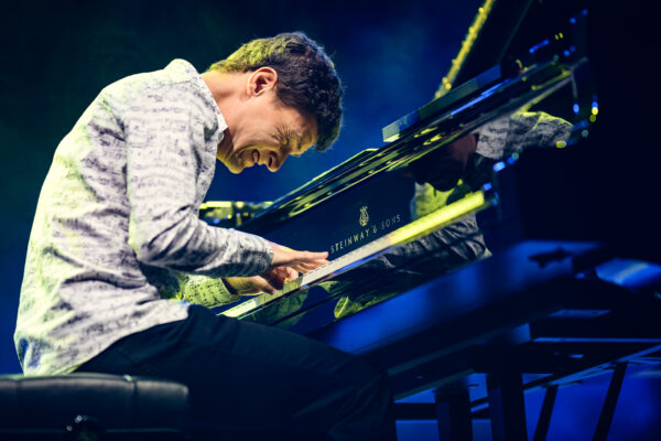 Mężczyzna w jasnej koszuli grający na fortepianie